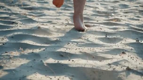 Las piernas de un hombre en forma cercana, corriendo descalzo sobre la arena caliente cerca del mar, en cámara lenta. Los deportes de verano corren en la playa. Estilo de vida saludable. Deportivas piernas haciendo ejercicio en una playa de corredor haciendo ejercicio . — Vídeo de stock