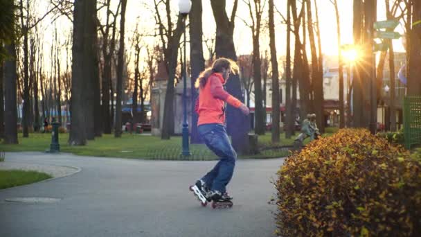 木を背景にした都心の公園で、秋のローラースケートで涼しいひげそりの男のスケートやダンス。アクティブなスポーツと健康的なライフスタイル。スローモーションでのサイドビュー. — ストック動画