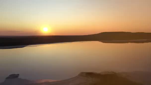 Bovenste luchtfoto van Koyashsky meer van boven tegen de achtergrond van de prachtige zonsondergang in de avond. De zon wordt weerspiegeld in het water. Rauwe zandkust. Opname van een mineraal zoutmeer in slow motion. — Stockvideo