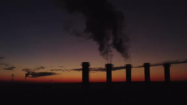 Chimeneas altas sobre el telón de fondo de la puesta del sol y la ciudad. El humo espeso sube alto. Silueta de cinco torres de refrigeración al atardecer. Casa de calderas de la ciudad por la noche. El sol se mueve sobre las chimeneas . — Vídeos de Stock