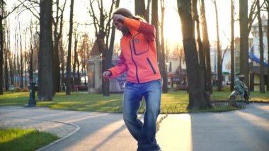 İyi esneme hareketleri olan havalı bir patenci, antrenman konilerinin arasında ustalıkla geriye doğru gider. Şehrin merkez parkında, güneşin altında, paten üzerinde ağır çekimde rahat bir eğitim..
