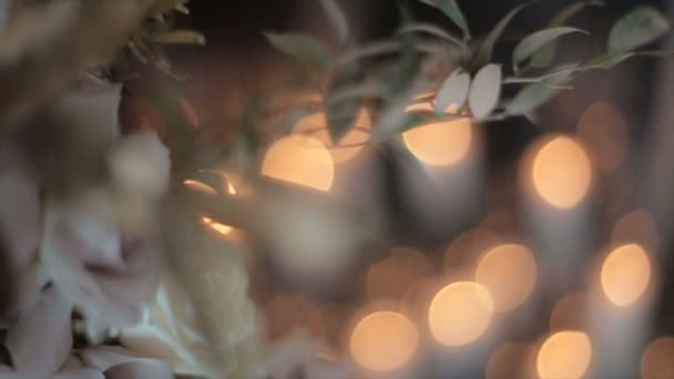 Belles roses blanches et crème pour le mariage des jeunes mariés sont debout dans un vase dans une forme étroite sur un fond de flou et scintillement éblouissement des bougies et des lumières de la lumière. Humeur festive — Video