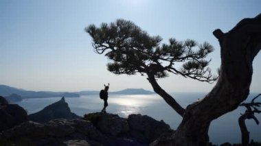 Dişi sporcu, boş bir gökyüzünde güzel, parlak bir güneşe ve bir uçurumun altında bulunan denize bakıyor ve doğanın tadını yavaş çekimde çıkarıyor. Sağlıklı bir yaşam tarzı ve dağlarda bir yolculuk fikri.