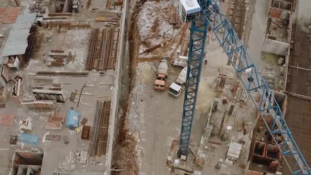 Hochkran für den Bau aus der Vogelperspektive sowie die Baustelle, auf der ein mehrstöckiges Gebäude entsteht. Blick von oben auf Betonmischwagen und eiserne Baumaterialien. — Stockvideo