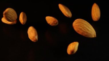 Appetizing almonds fall down on a black background. A handful of crispy nuts sprinkles on a dark smooth table. Edible beneficial seed kernels scatter on a black surface. One of the favorite treats.