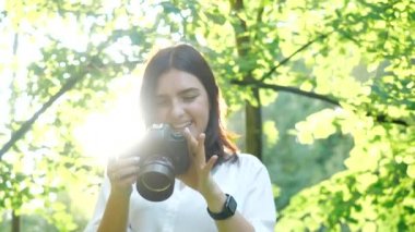 Mutlu güzel kız az önce profesyonel bir kamerada çekilen fotoğraflara bakıyor. Güneşli bir yaz parkında çekilen fotoğrafları izleyen gülümseyen genç bir fotoğrafçının yakın görüntüsü..