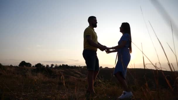 Älskade unga par flicka och kille hålla händer, flirta kyss och krama på fältet mot bakgrund av gryningen i slow motion. Glad och romantisk relation. Datum på fältet vid solnedgången bakgrund. — Stockvideo