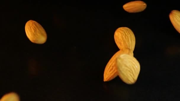 Close-up shooting of crumbling appetizing almonds on a black background. Flying almond kernels fall on a black table. Tasty and healthy nut. Seed kernels roll in handfuls down. Plum tree. Great snack. — Stok video