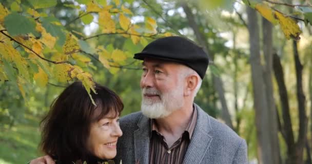 Vue de face d'un couple âgé heureux et joyeux dans un parc de la ville confortable à l'automne, qui sont câlins et se reposent à l'extérieur dans la rue parmi les arbres et l'herbe. Vue rapprochée d'un homme et d'une femme âgés . — Video