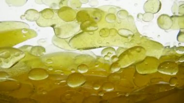 Beautiful grape seed oil settles on the surface of a white background liquid. Fragrant and tasty walnut oil flows around the container, close-up view. Golden liquid with bubbles and drops of air.