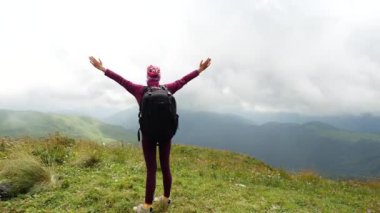 Middle view from the back of a woman tourist who stands near a cliff of a mountain and raises her hands from enjoying the beauty of the landscape from a height in Adygea, Russia.