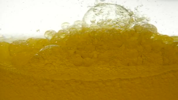 Golden refined vegetable oil is slowly stirred against a white moving background, creating a bubble structure of air. Close-up view of olive oil in container. Focus of yellow oil in transparent bowl. — Αρχείο Βίντεο