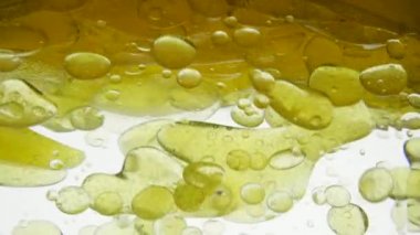 Bright colored air bubbles on background of golden oil. Yellow liquid is poured into a container, close-up view. Different density of the liquid, fat molecules do not mix with water. Focus boiling oil