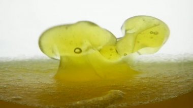 Fıstık yağı, beyaz arka planda susam yağıyla karıştırılmış değerli ve sağlıklı bir yemektir. Sarı hareket eden arka planda geniş ve küçük hava kabarcıklarının yakın görüntüsü. Altın yağın tortusu bir konteynırda.