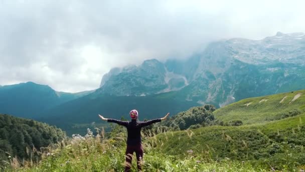 Активная женщина наслаждается и любуется прекрасным видом на горы Кавказа, стоящие у скалы, Адыгея, Россия. Обратная съемка туриста, стоящего на краю горы в солнечную погоду . — стоковое видео