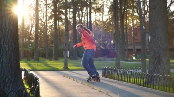 Een sportman doet rolschaatstraining in het centrale park van de stad tussen de bomen op een zonnige herfstdag, het uitvoeren van complexe bochten tussen de kegels in slow motion. Actieve gezonde vrijetijdsbesteding. — Stockvideo
