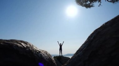 Ukrayna 'nın Kırım, Karaul-Oba Dağı' nın tepesine tırmanan genç bir kızın taşları arasında ateş etmek. Atletik kadın kollarını kaldırır, denize bakar ve parlak güneşin ışınlarını yakalar..