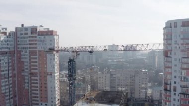 Aerial landscape of the construction of a new modern building for people to live in the background of residential buildings in Kharkov, Ukraine. Construction cranes workers on the roof, top view.
