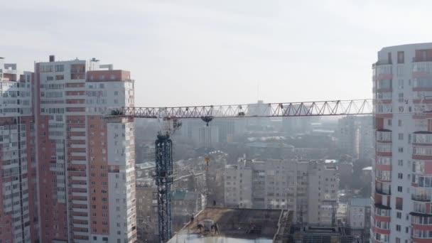 Paesaggio aereo della costruzione di un nuovo edificio moderno per le persone a vivere sullo sfondo di edifici residenziali a Kharkov, Ucraina. Gru da costruzione lavoratori sul tetto, vista dall'alto . — Video Stock