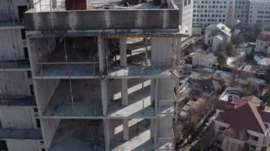 Aerial shot from the side of a multi-storey residential building during construction in sunny weather. Side view of the unfinished floors of a high-rise building against the backdrop of the city.