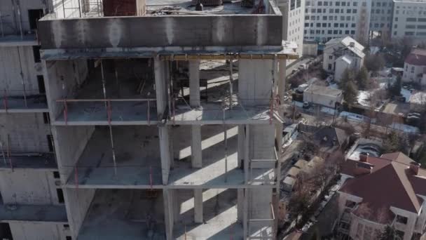 Vue aérienne du côté d'un immeuble résidentiel de plusieurs étages pendant la construction par temps ensoleillé. Vue latérale des étages inachevés d'un immeuble de grande hauteur dans le contexte de la ville . — Video