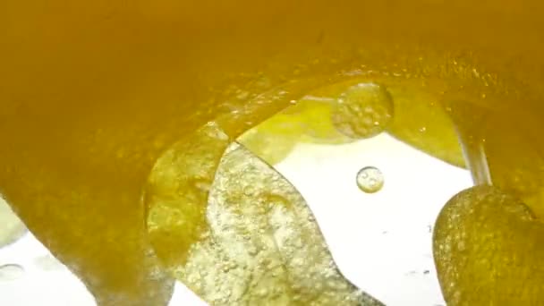 Close-up zicht op gouden vloeistof in een container. Vloeibare gele golflijn. Gouden luchtbellen. Voor het project, rust, olie, honing, bier, sap, shampoos of andere succesvolle opties. Op witte achtergrond. — Stockvideo