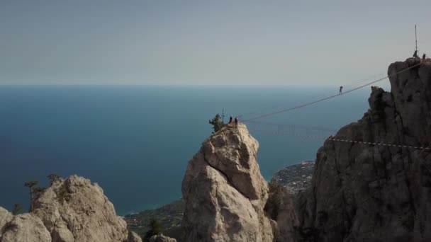 クリミア半島で最も高い山の空中撮影- Ai-Petri 。黒海、ヤルタの暖かい春の季節の背景に極端な橋の上の山のピークに観光客が上昇します. — ストック動画