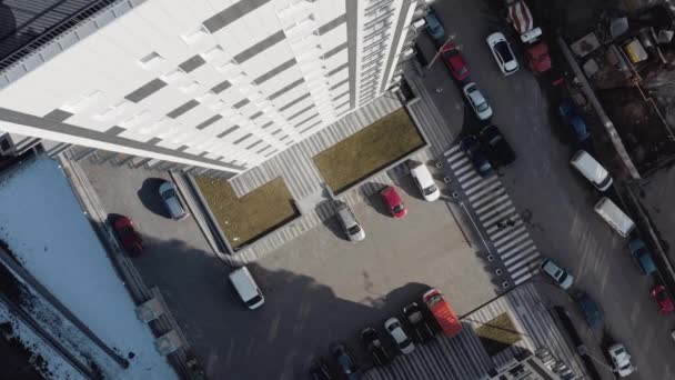 Plan circulaire vertical d'un parking avec de nombreuses voitures près d'un immeuble résidentiel blanc à plusieurs étages en hiver. Vue de dessus de la cour avec parking et passage piéton par temps ensoleillé . — Video