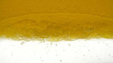 Sunflower oil is poured into a glass container. Close-up view of bio fuel shot in a research laboratory. A golden background of poured sesame oil and black cumin oil, resulting in bubbles and bulbs.