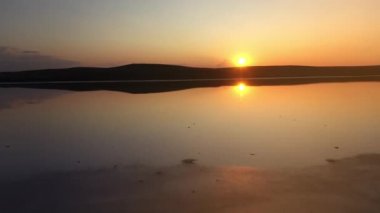 Kayashsky Gölü 'nün üzerinden parlak ve güzel bir günbatımının arka planına doğru uçuyor. Kırım, Ukrayna 'da gölün havadan çekilmiş görüntüsü, üst görüntü, yavaş çekim. Güneş suya yansıyor..