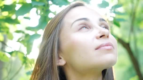 Rostro de una hermosa mujer joven, vista de cerca sobre un fondo de árboles y el sol en un acogedor parque de la ciudad. Muchacha modelo atractiva con ojos verdes se fotografía para una revista. Fotosesión en la calle . — Vídeo de stock