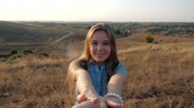 Close shot of a pretty young girl who holds her boyfriends hand in the background of the bright sun. Close-up view of smiling and cheerful style girl follow me. Beautiful woman on sunset background.