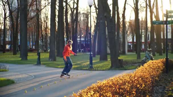 Een ervaren rolschaatser in het park, rijdt vakkundig achteruit, kruist benen. Actieve en sportieve man voert professioneel rolschaatsen in een gezellig stadspark. Gezond ontspannen in slow motion. — Stockvideo