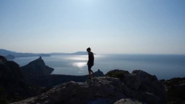 Cesur genç kız bir uçurumun tepesinde yürüyor ve denizin en güzel manzarasını ve üzerindeki en parlak güneşi yavaş çekimde seyrediyor. Atletik kadın turist yüksek bir uçurumun tepesine tırmanıyor..