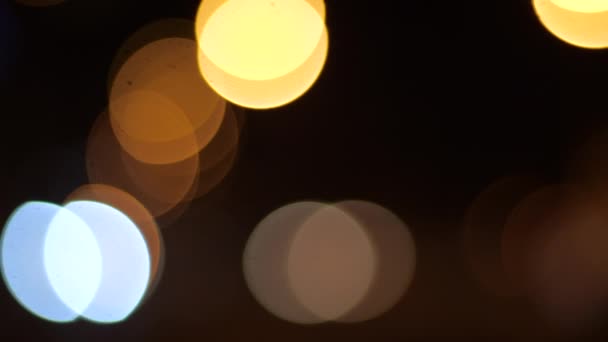 Círculos excavados de luz parpadean sobre el fondo de la ciudad oscura de la tarde. Brillante resplandor de luz amarilla, naranja y azul en la oscuridad por la noche. Brillante deslumbramiento borroso de luces parpadear . — Vídeo de stock