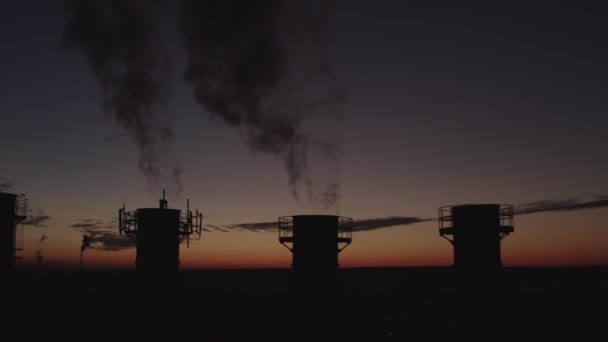 Chimeneas altas sobre el telón de fondo de la puesta del sol y la ciudad. El humo espeso sube alto. Silueta de cinco torres de refrigeración al atardecer. Casa de calderas de la ciudad por la noche. El sol se mueve sobre las chimeneas . — Vídeo de stock