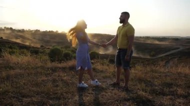 Side view of a cute and beautiful couple in love on the field. A nice girl slowly approaches her boyfriend, hugs him and kisses him. A romantic day for two lovers in love under the bright spring sun.