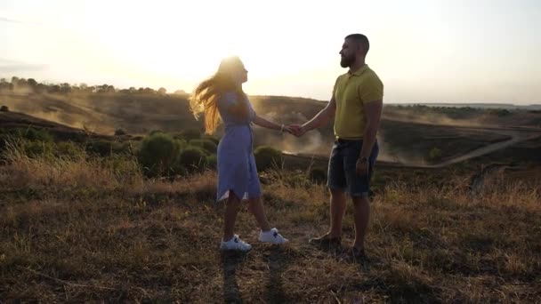 Side view of a cute and beautiful couple in love on the field. A nice girl slowly approaches her boyfriend, hugs him and kisses him. A romantic day for two lovers in love under the bright spring sun. — Stockvideo