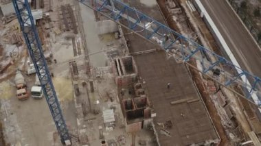 Kuş bakışı bir inşaat için yüksek vinç ve çok katlı yeni bir binanın inşa edildiği şantiye. Beton karıştırıcı kamyonların ve demir yapı malzemelerinin üst görünümü.