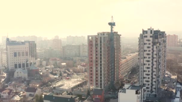 Processen att bygga en ny modern flervåningsbyggnad i staden under vintersäsongen. Flygfoto av blå konstruktion kran och byggnad tak mot bakgrund av bostäder låga hus. — Stockvideo