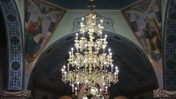 Kharkiv, Ukrajna - 05.10.2019: Bottom up shot of a beautiful yellow gilded chandelier of a church dome inside. Különböző imaképek és feliratok a kolostor mennyezetén. — Stock videók