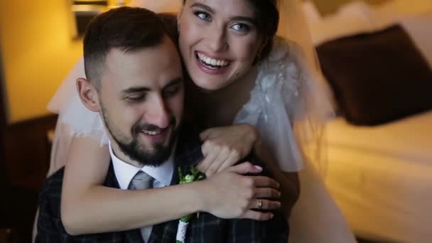 Όμορφη γλυκιά νύφη σε ένα λευκό νυφικό χαμόγελα αγκαλιάζει αγαπημένο γενειοφόρος γαμπρός της κάθεται σε μια καρέκλα. Ευτυχισμένο γαμήλιο ζευγάρι απολαμβάνουν μήνα του μέλιτος στο διάσημο και πολυτελές ξενοδοχείο Kharkov Palace, Ουκρανία. — Αρχείο Βίντεο