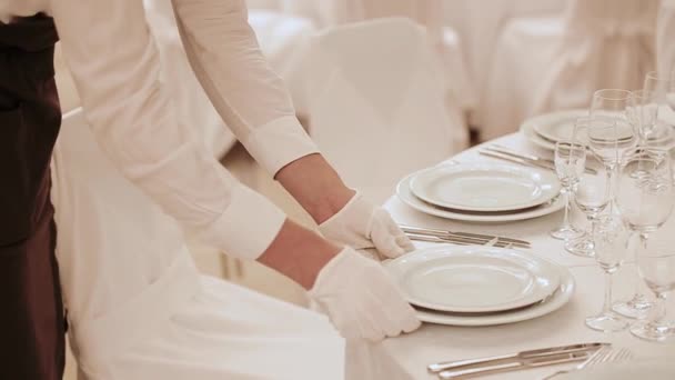 O garçom de luvas brancas perfeitamente monta uma mesa de casamento. O garçom profissional move-se e endireita chapas e utensílios de comida em uma mesa de banquete de uma festa. Pessoal de serviço. Feliz dia da noiva e do noivo . — Vídeo de Stock