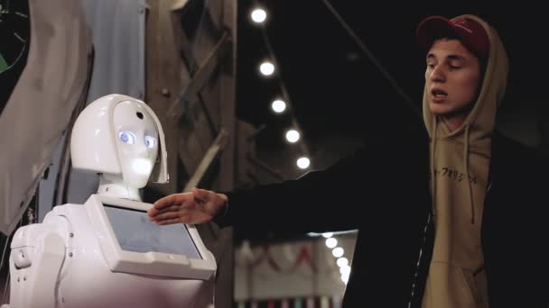 Kharkiv, Ucrânia - 09 de novembro de 2019: Um gesto de guia masculino, fala sobre uma garota robô KIKI em uma exposição interativa, demonstra. Tecnologias robóticas científicas modernas. Inteligência artificial — Vídeo de Stock