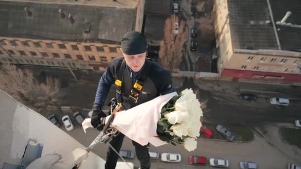 Втратити вигляд чоловіка професійного альпініста в уніформі, що звисає на висоті над багатоповерхівкою з красивим букетом білих троянд. Кур'єрський альпініст доставляє квіти до вікна. Р-подібні — стокове відео