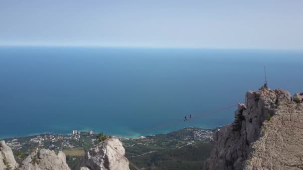 Aerial shot of the top of the mountain Ai-Petri, Yalta, Ukraine. A pair of tourists walking to the top of the mountain on a wooden bridge to a peak in Crimea. Entertainment. Stepping over the abyss. — Stock Video