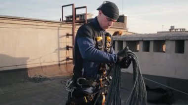 Üniformalı endüstriyel tırmanışçı yüksek binaların çatısında duruyor ve aşağıdaki bina için uzun güvenlik ipini eline alıyor. Radikal adam tehlikeli işlere bulaşmış ve risk altında..