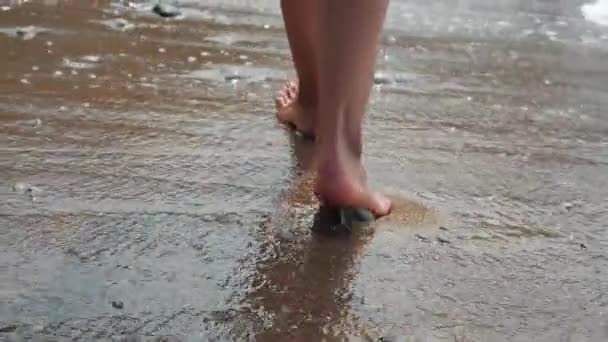 Widok z bliska pięknych kobiecych stóp idących do przodu wzdłuż piankowych fal morza wzdłuż piaszczystego brzegu. Smukłe i seksowne nogi dziewczyny stąpają po piasku brzegu wzdłuż ekscytującego oceanu. — Wideo stockowe