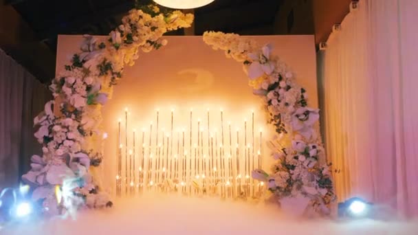 Hermoso altar de boda decorado con flores blancas iluminadas por bombillas de color amarillo brillante, en el que el vapor de los focos vuela en acogedor salón abovedado cerrado para la ceremonia de boda de la novia y el novio . — Vídeos de Stock