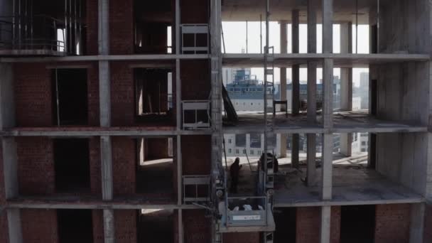 Side view of construction through the floors of new multi-story residential building. Active development of high-rise buildings of city. Professional builders and crews erect a skyscraper in winter — Stock Video